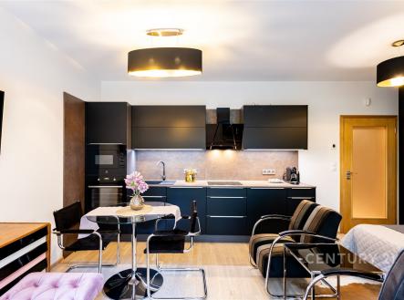 Moderní kuchyň s černými skříňkami, parketová podlaha a vestavěné spotřebiče, otevřený prostor s jídelním koutem a moderním osvětlením. | Pronájem bytu, 1+kk, 37 m²