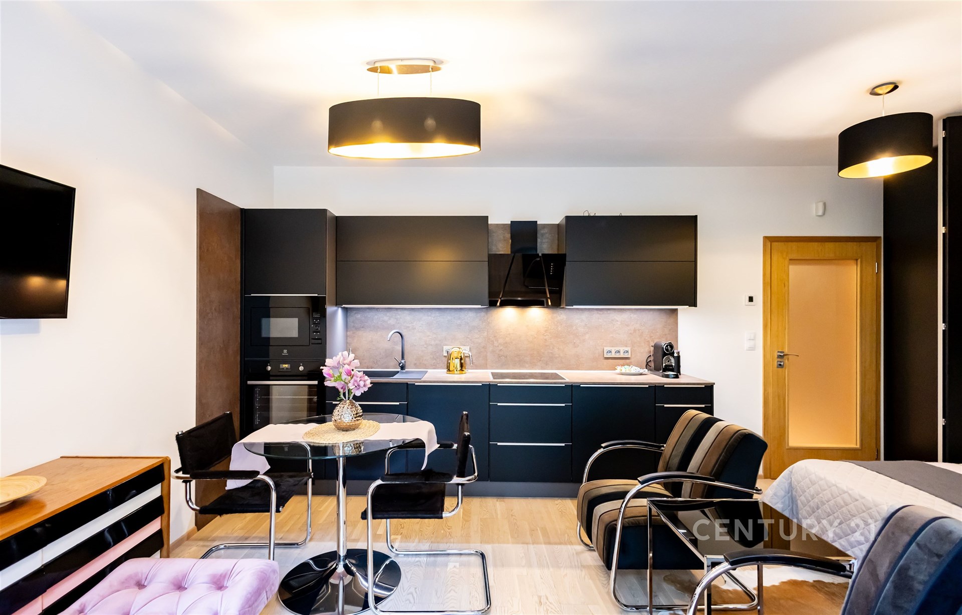 Moderní kuchyň s černými skříňkami, parketová podlaha a vestavěné spotřebiče, otevřený prostor s jídelním koutem a moderním osvětlením.