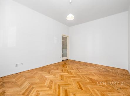 Prázdný pokoj s parketovou podlahou, bílými stěnami a moderním osvětlením. Vstupní dveře s prosklením zajišťují světlo do prostoru. | Prodej bytu, 2+kk, 49 m²