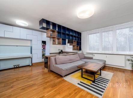 Světlý obývací pokoj s parketovou podlahou, velkými okny a moderní vestavěnou knihovnou, působí prostorně a elegantně. | Prodej bytu, 2+kk, 78 m²
