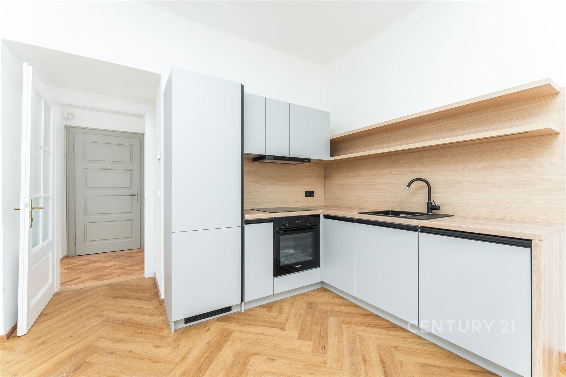 Moderní kuchyň s parketovou podlahou, vestavěnými spotřebiči a světlými dřevěnými povrchy, nabízí elegantní a praktický design.