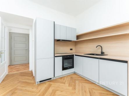Moderní kuchyň s parketovou podlahou, vestavěnými spotřebiči a světlými dřevěnými povrchy, nabízí elegantní a praktický design. | Prodej bytu, 3+kk, 75 m²