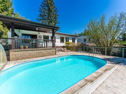 Bazén na slunné terase s dlažbou, obklopený moderní rodinnou vilou. Nabízí relaxaci a soukromí v klidné lokalitě s výhledem na zeleň. | Prodej - dům/vila, 110 m²