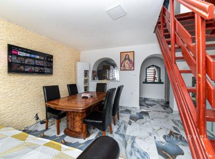 Jídelní kout s mramorovou dlažbou, dekorativní kamennou stěnou a dřevěným stolem. Kovové schody vedou do patra, vytváří moderní atmosféru. | Prodej bytu, 3+1, 98 m²