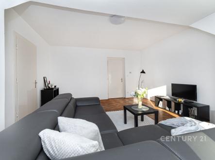 Světlý obývací pokoj s parketovou podlahou, moderní sedačka, velká okna, minimalistický design, černý nábytek, útulný prostor. | Prodej bytu, 2+1, 192 m²