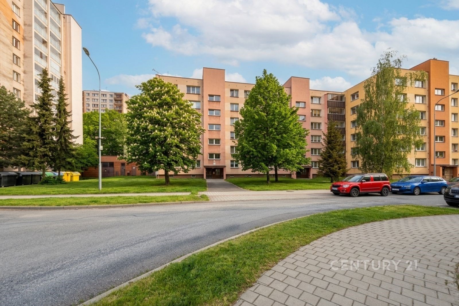 Vícepatrový bytový dům s novou fasádou, obklopen zelení a stromy, nachází se na klidné ulici v dobře dostupné lokalitě.