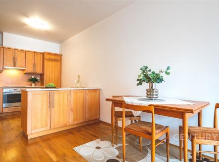Kuchyň s dřevěnou podlahou a moderními skříněmi, jídelní stůl v rohu, světlé prostory. | Prodej bytu, 2+kk, 72 m²