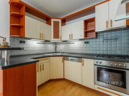 Moderní kuchyň s dřevěnými skříňkami, vestavěnou troubou a dlaždičkovým obkladem, parketová podlaha vytváří elegantní interiér. | Prodej bytu, 3+1, 75 m²