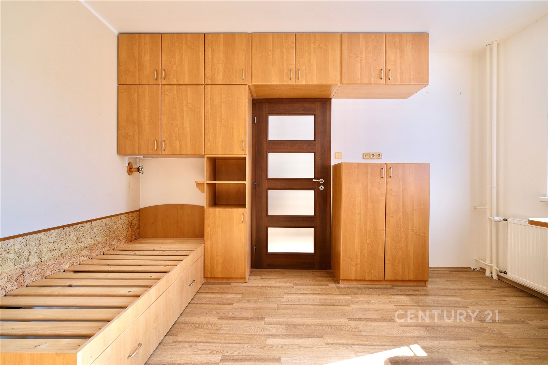 Prostorná ložnice s dřevěnými vestavěnými skříněmi, moderními dveřmi a parketovou podlahou, ideální pro uspořádané skladování.