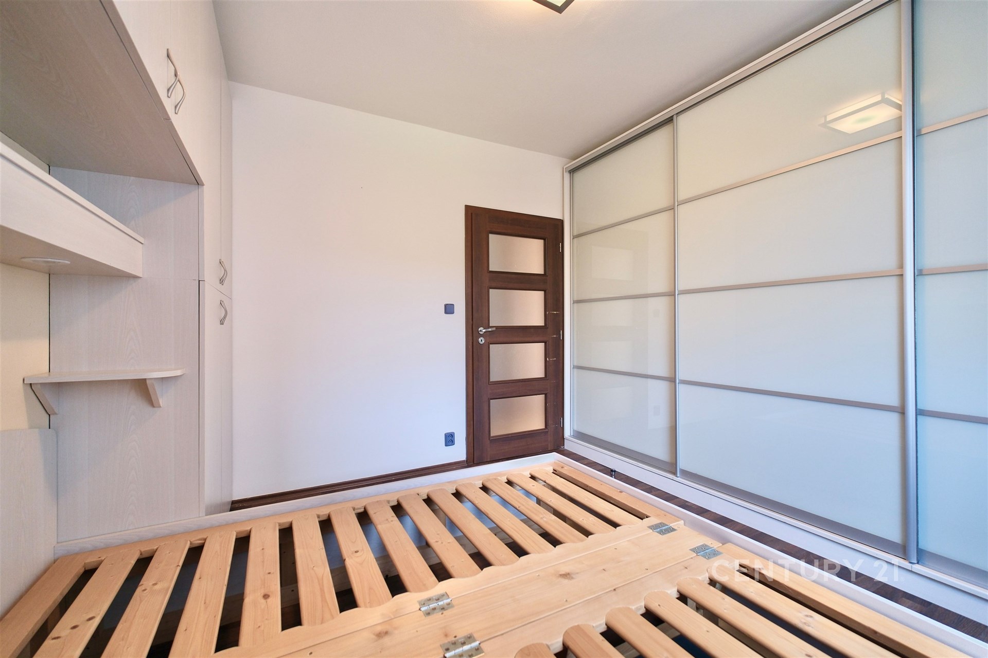 Ložnice s vestavěnými skříněmi, parketovou podlahou a moderními posuvnými dveřmi, ideální pro světlý a funkční interiér.