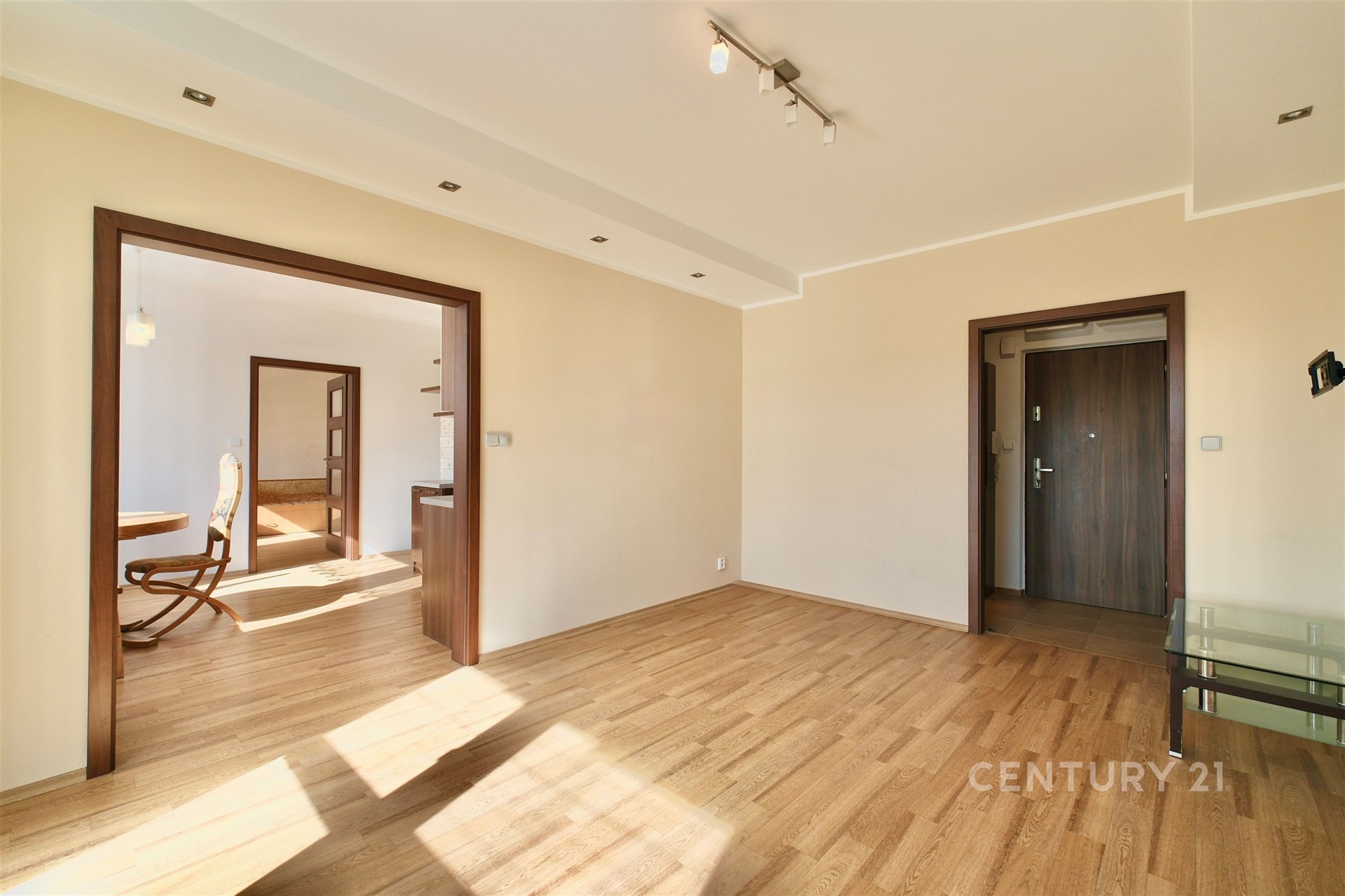 Světlý obývací pokoj s parketovou podlahou, moderním osvětlením a velkými okny, které poskytují dostatek přirozeného světla.