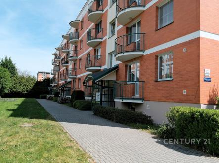 Červená cihlová fasáda moderního bytového domu s balkonem a zámkovou dlažbou, udržovaný trávník a zahrada, klidná lokalita. | Pronájem bytu, 2+kk, 60 m²