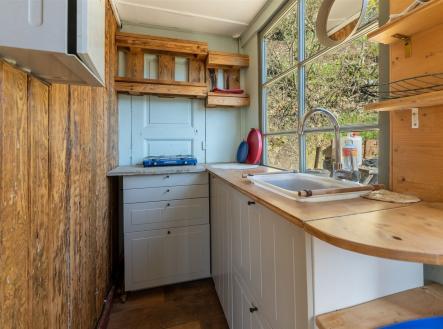 Kompaktní kuchyň s dřevěnými prvky, světlou linkou a velkými okny. Stylová dlažba a rustikální design dodávají útulný pocit. | Prodej - dům/vila, 47 m²