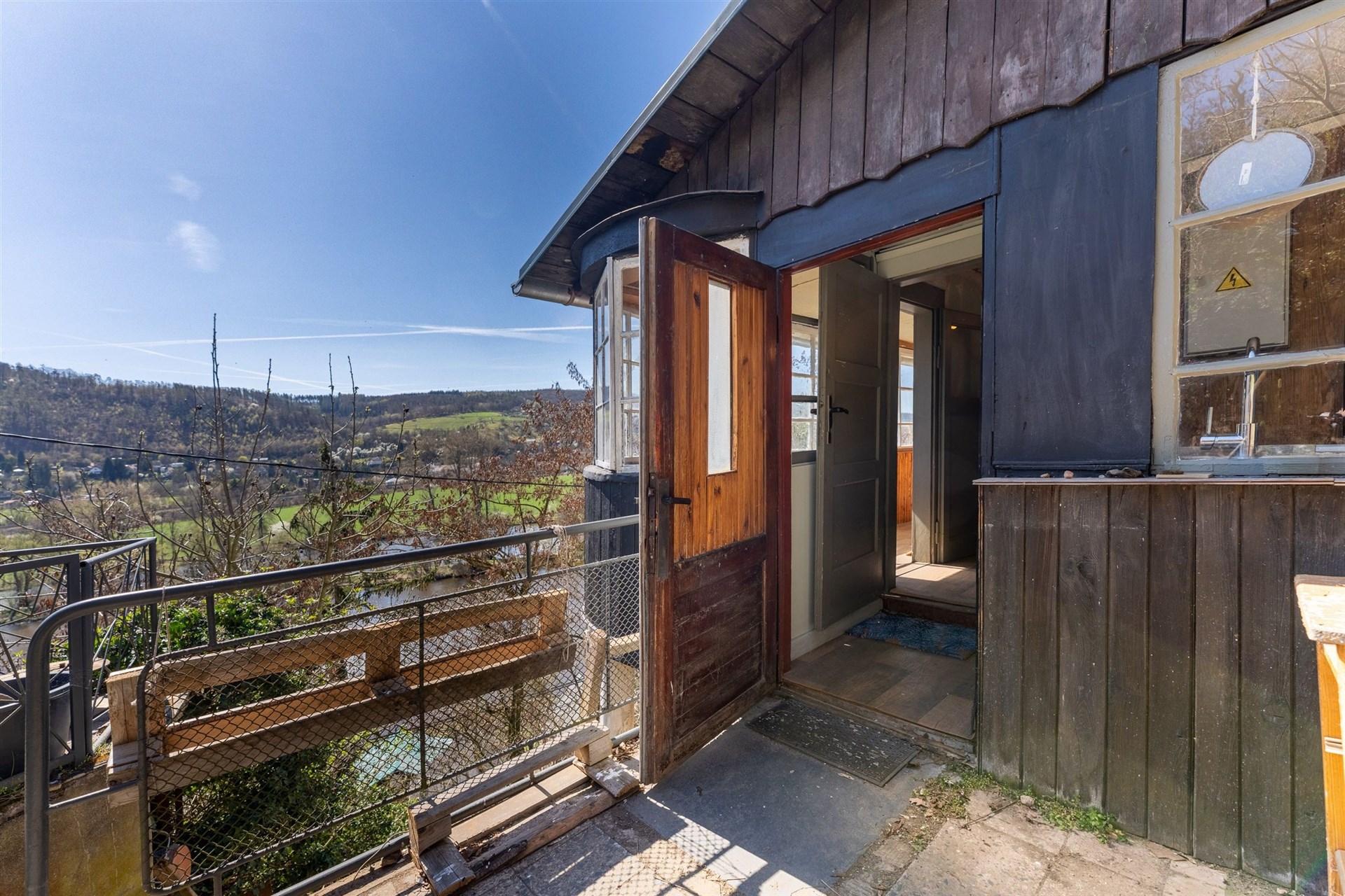 Venkovní terasa s dřevěnou podlahou a výhledem na krajinu, ideální pro relaxaci, útulný styl, původní dřevěné obložení stavby.