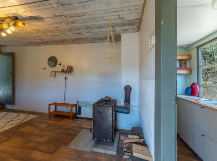 Venkovský obývací pokoj s dřevěnou podlahou, krbovými kamny a velkými okny. Strop z dřevěných prken dodává rustikální atmosféru. | Prodej - dům/vila, 47 m²