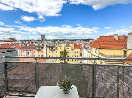 Balkon s kovovým zábradlím a výhledem na město, světlé cihlové budovy s červenými střechami, modrá obloha s mraky | Pronájem bytu, 4+kk, 102 m²