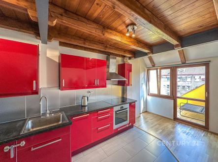 Moderní kuchyň s červenými lesklými skříňkami, dřevěným stropem a parketovou podlahou, velká okna poskytují dostatek světla | Pronájem bytu, 4+kk, 102 m²
