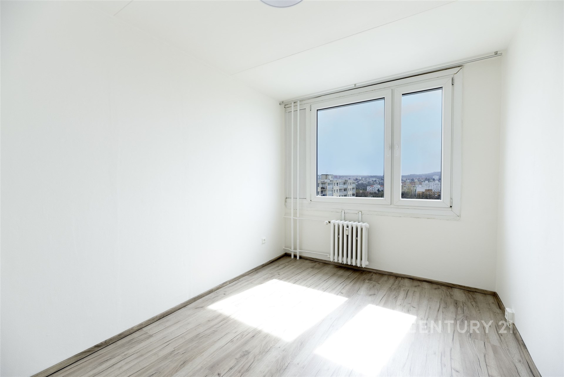 Světlý pokoj, moderní podlahy s dřevěným vzhledem, velká okna s výhledem, minimalistický styl.