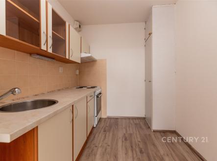 Úzká kuchyň s parketovou podlahou, dřevěnými skříňkami a světlou pracovní deskou, moderní keramická dlažba na zdi kolem sporáku. | Pronájem bytu, 2+kk, 41 m²
