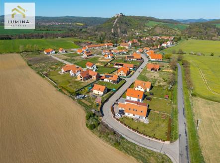 Letecký pohled na novou rezidenční čtvrť s moderními domy s červenými střechami, obklopenou zelenými poli a malebnou krajinou. | Prodej - pozemek pro bydlení, 821 m²