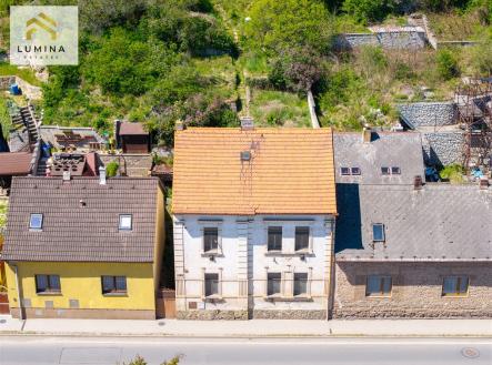 Starší rodinný dům s červenou střechou, vedle dalších dvou domů, zasazený v zelené zahradě. Potenciál pro rekonstrukci a renovaci. | Prodej - pozemek pro bydlení, 2 234 m²