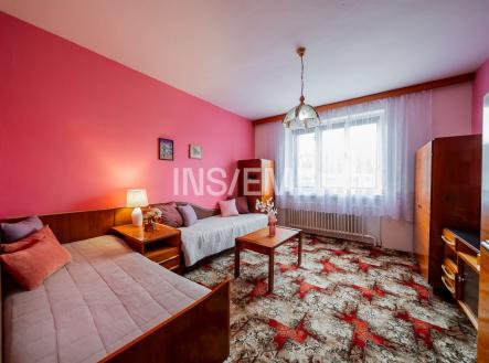 Světlý obývací pokoj s retro kobercem, dřevěným nábytkem a velkým oknem, které propouští dostatek přirozeného světla. | Prodej - dům/vila, 152 m²