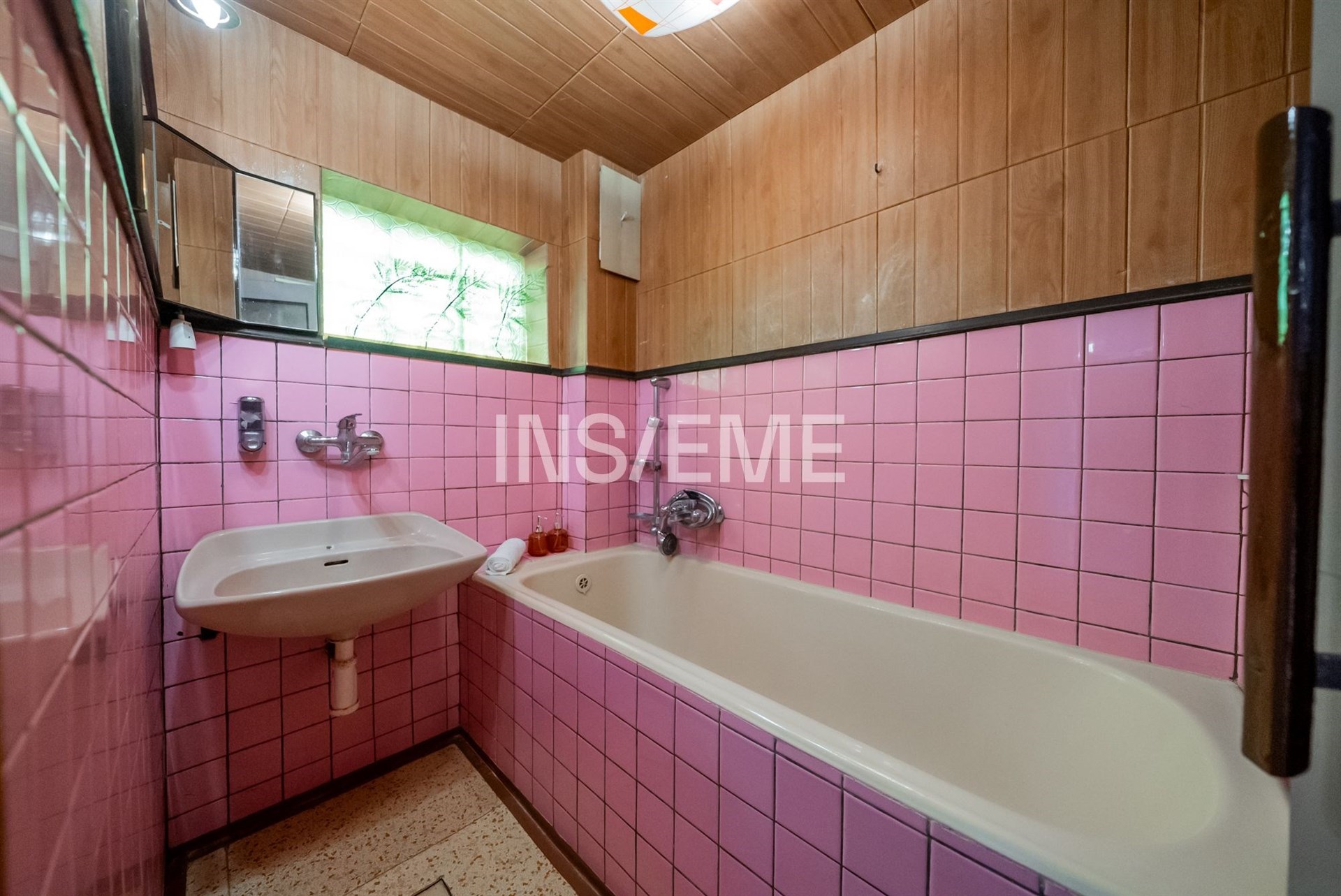 Koupelna s růžovými dlaždicemi, vanou a umyvadlem; dřevěné obložení dodává retro styl, původní zachovalý stav.