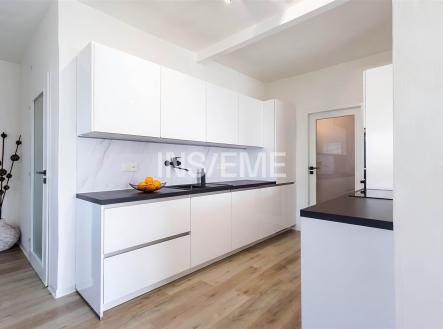 Moderní kuchyň s bílými skříňkami, černou pracovní deskou a parketovou podlahou, prostorná a světlá s minimalistickým designem. | Prodej - dům/vila, 250 m²