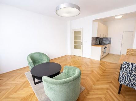 Světlý obývací pokoj s parketovou podlahou, moderní kuchyňskou linkou a velkými okny. Prostor je světlý a přehledný. | Pronájem bytu, 1+kk, 30 m²