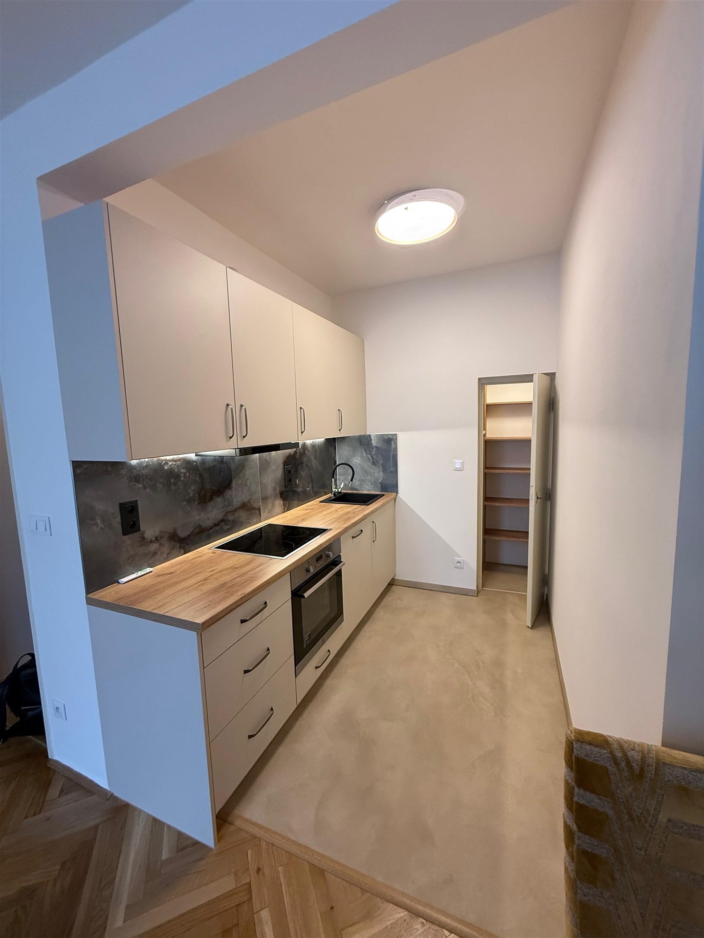 Kompaktní moderní kuchyň s dřevěnou pracovní deskou, vestavěnými skříněmi a parketovou podlahou, ideální pro efektivní využití prostoru.