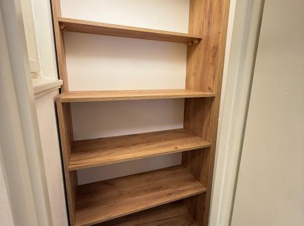 Úložná komora s dřevěnými policemi, minimalistický design, světlé stěny, ideální pro efektivní organizaci v moderním interiéru. | Pronájem bytu, 1+kk, 30 m²