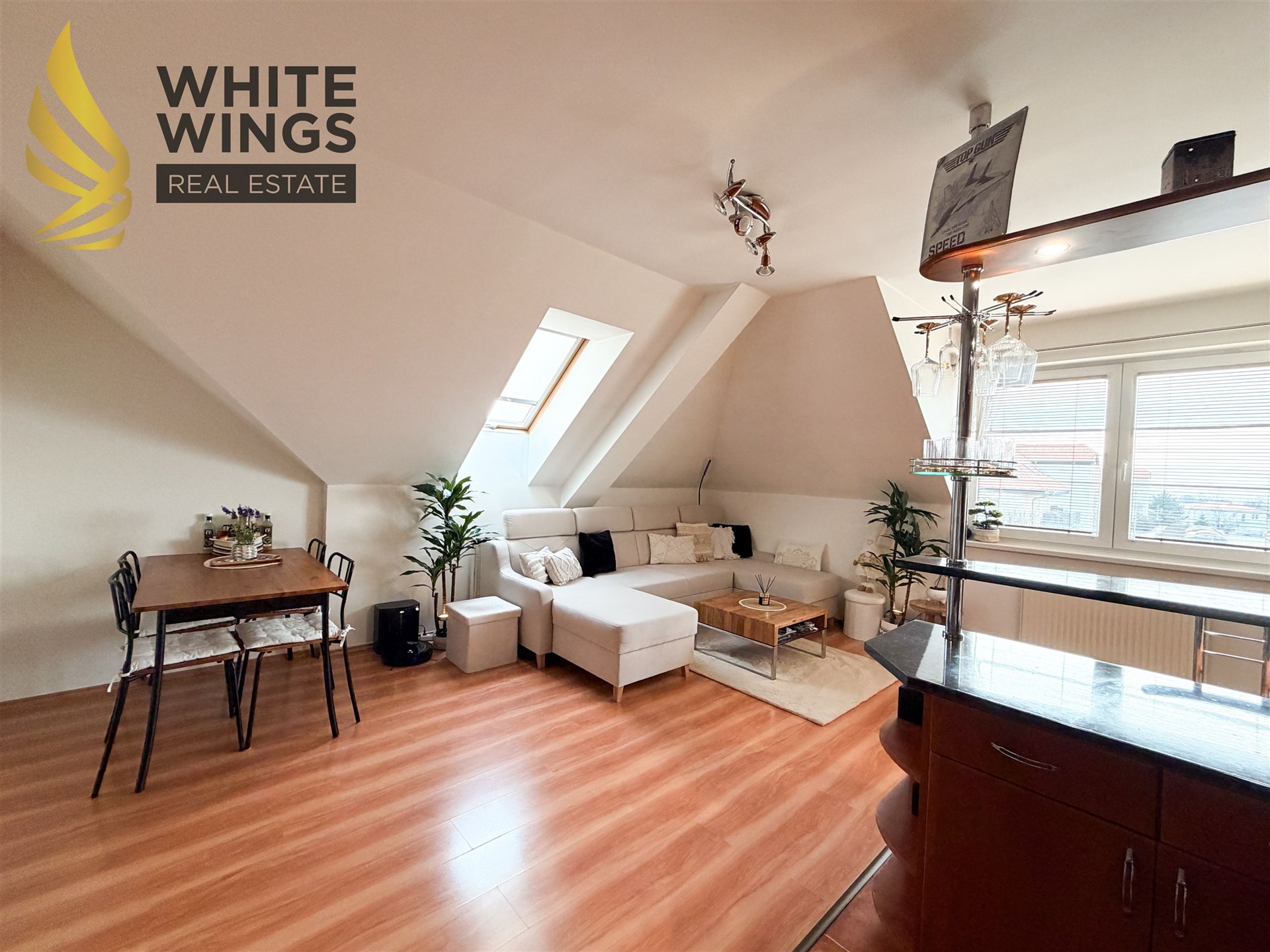 Podkrovní obývací pokoj s parketovou podlahou a velkými střešními okny, moderní nábytek a stylové osvětlení vytváří útulnou atmosféru.