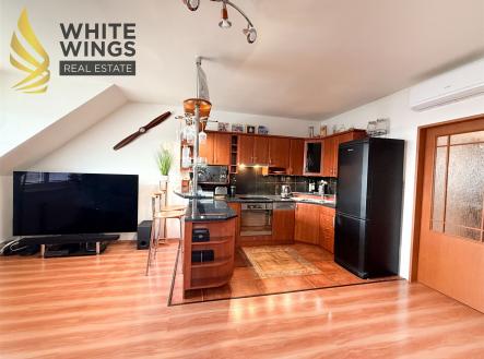 Podkrovní kuchyň s moderními spotřebiči, dřevěnými skříňkami a parketovou podlahou, vedle obývacího prostoru s velkou televizí. | Prodej bytu, 3+kk, 87 m²