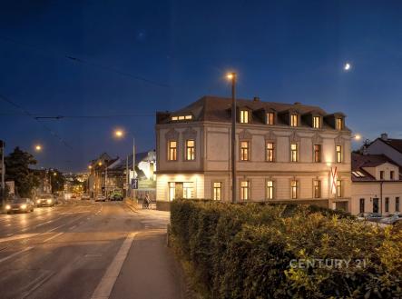 Historická budova v nočním osvětlení, nacházející se na rohu ulice. Budova má klasickou fasádu a velká osvětlená okna. | Prodej - skladovací prostor, 85 m²