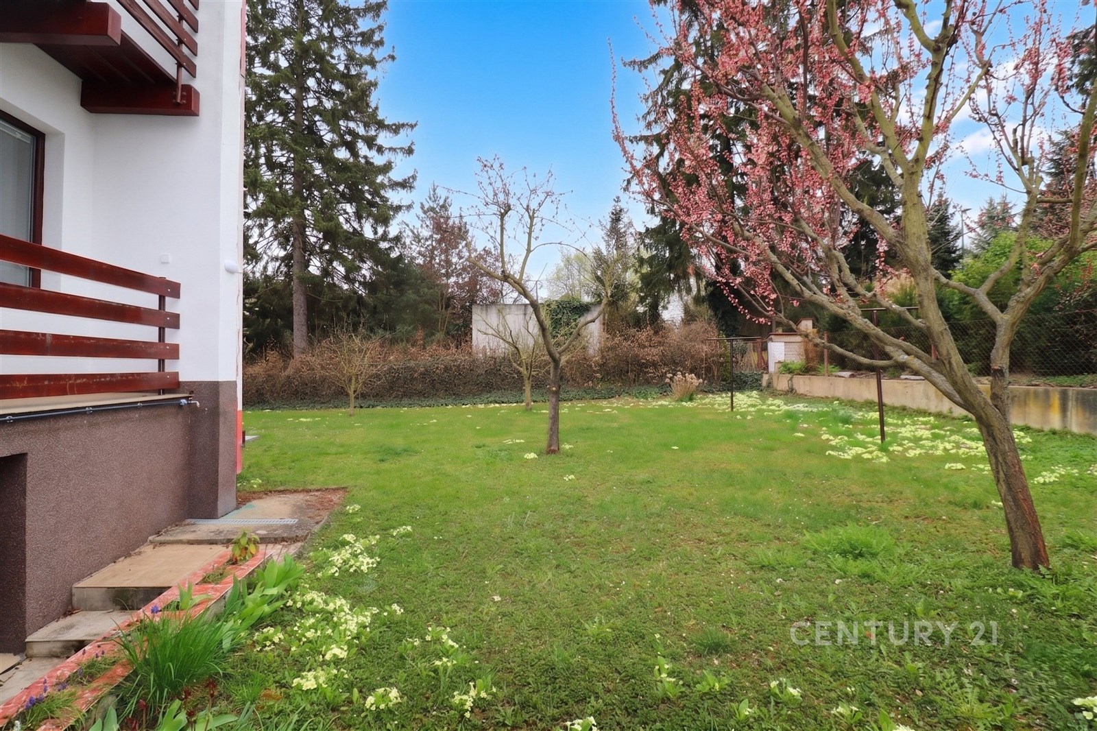Zahrada s udržovaným trávníkem, kvetoucími stromy a živým plotem, nabízí klidné prostředí. Vhodná pro rodinné aktivity a relaxaci.