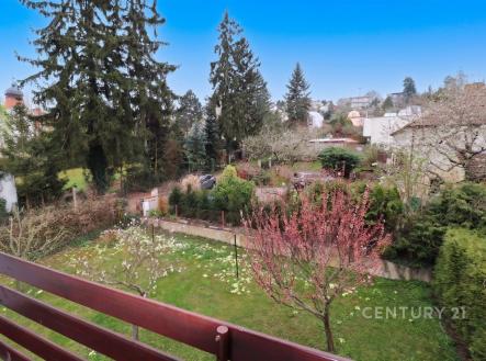 Výhled z balkonu na zahradu s ovocnými stromy, vzrostlé jehličnany a udržované keře, poskytující poklidné a zelené prostředí v rezidenční čtvrti. | Pronájem - dům/vila, 234 m²