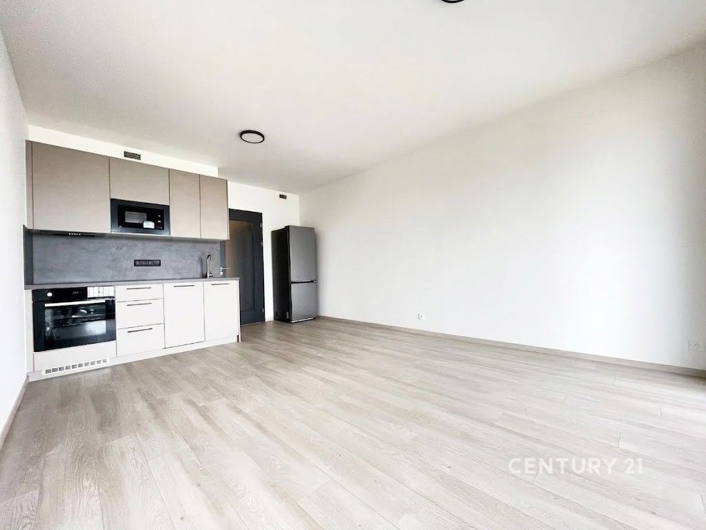 Světlý obývací pokoj s moderní kuchyní, parketová podlaha, vestavěné spotřebiče, minimalistický design, vhodné pro mladé rodiny.