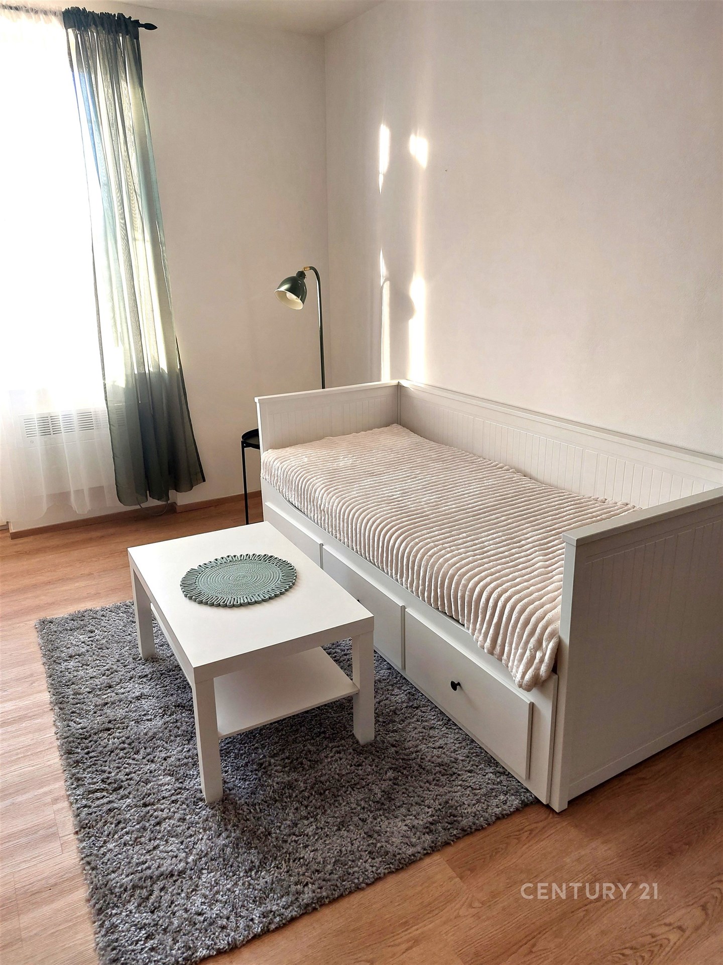 Světlý obývací pokoj s parketovou podlahou, velkými okny a moderním nábytkem.