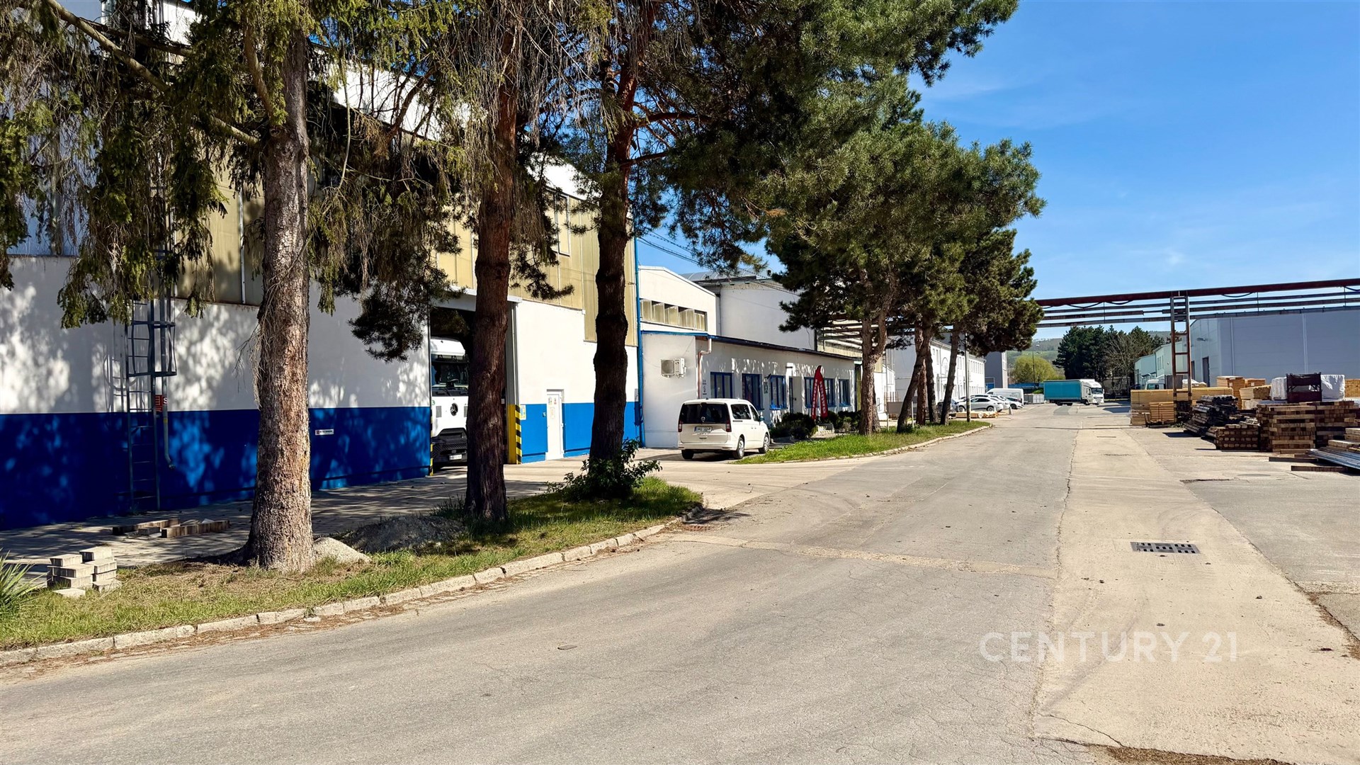 Průmyslová zóna s asfaltovou cestou, sklady a administrativními budovami, ideální pro logistické účely, dobrý přístup a manipulace s materiálem.