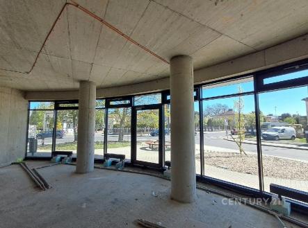 Rozestavěný interiér s velkoplošnými okny, betonovými stěnami a stropem. Světlý prostor nabízí možnost moderního designu v renovaci. | Prodej - obchodní prostor, 84 m²