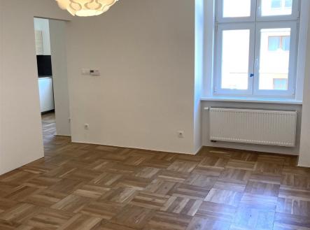 Světlý obývací pokoj s parketovou podlahou, velkými okny a moderním osvětlením, ideální pro komfortní bydlení. | Pronájem bytu, 1+1, 43 m²