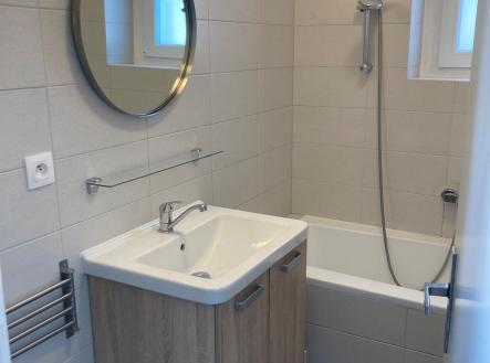 Koupelna s moderními obklady, vanou a dřevěnou skříňkou pod umyvadlem, nabízí elegantní styl a praktické využití prostoru. | Pronájem bytu, 1+1, 43 m²