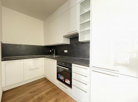 Moderní kuchyň s lesklými bílými skříňkami, vestavěnými spotřebiči a dřevěnou podlahou, nabízí elegantní prostor pro vaření. | Pronájem bytu, 2+kk, 41 m²