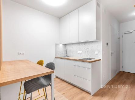 Kompaktní kuchyň s moderním nábytkem, bílými skříňkami a dřevěnou podlahou, doplněná světlým obkladem a jídelním koutem pro dva. | Prodej bytu, 1+kk, 32 m²