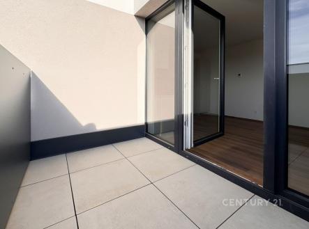 Balkon s dlažbou a velkými okny, které vedou do světlého obývacího pokoje s parketovou podlahou, moderní design a otevřený prostor. | Pronájem bytu, 2+kk, 44 m²