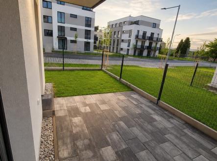Terasa s moderní dlažbou nabízí ideální místo k relaxaci, s výhledem na okolní architektonicky střízlivé budovy a upravený trávník. | Prodej bytu, 1+kk, 39 m²