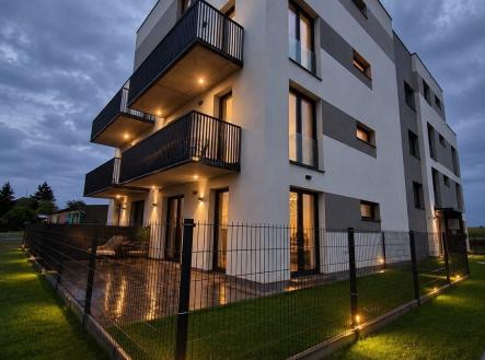 Moderní bytový dům s velkými balkony a světlou fasádou, oplocená zahrada a kvalitní večerní osvětlení, klidná rezidenční čtvrť | Prodej bytu, 1+kk, 39 m²