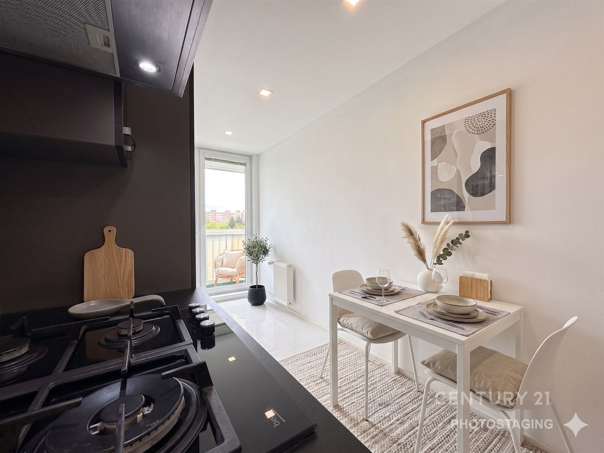 Kompaktní jídelní kout s moderním nábytkem, světlou dlažbou a velkým oknem. Minimalistický styl a světlé vybavení vytvářejí elegantní atmosféru.