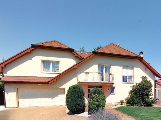 Velký rodinný dům s balkonem, červenou střechou a upravenou zahradou, nabízí klidné bydlení na okraji města.