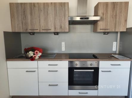 Moderní kuchyň s dřevěnými skříňkami, vestavěnou troubou a skleněným obkladem, vybavená varnou deskou a digestoří. | Pronájem bytu, 2+kk, 52 m²